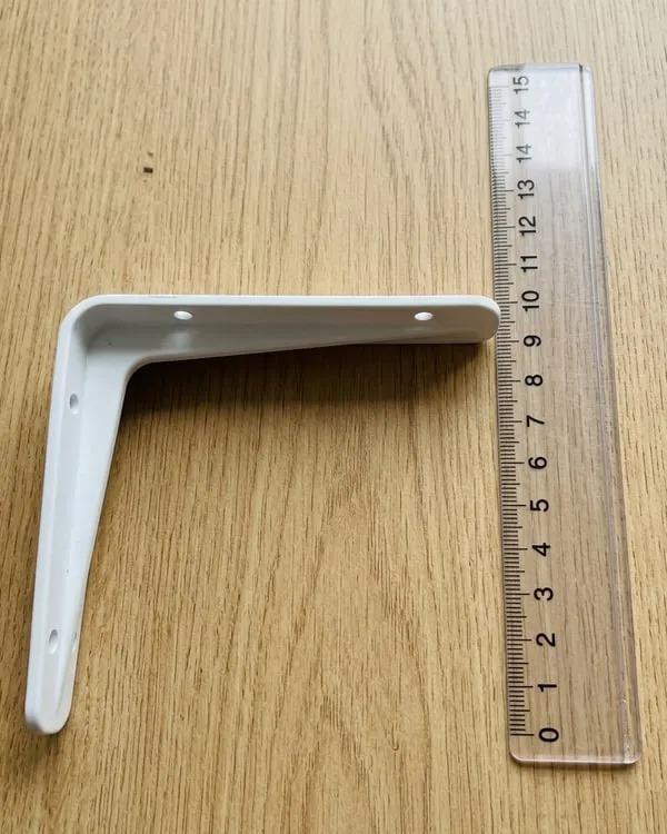 Bijeli plastični nosač u obliku slova L na drvenom stolu, pored providnog lenjira od 15 cm